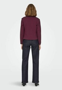 Veste bordeaux au design ajusté, avec de larges revers et des manches longues, associée à un jean en denim foncé taille haute à coupe droite.