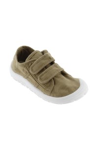 Zapato de lona caqui con suela de goma blanca, punta redondeada y dos bandas de velcro. Presenta detalles de costura y una superficie de tela texturada.