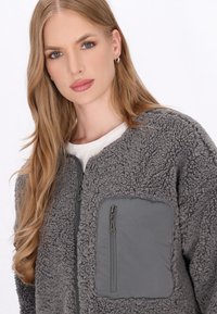 Grau Fleece-Jacke mit strukturierten Oberflächen, einer Reißverschlusstasche auf der Brust und glatten Akzenten. Reißverschluss und Stehkragen-Design.