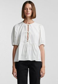 Hvit bluse med puffermer, rund halslinning og frontåpning, bundet med sløyfer, rynket midje og lett stoff.