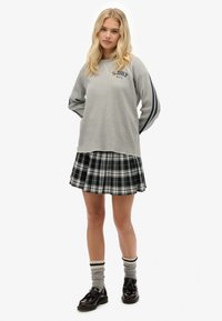 Sudadera gris con rayas azul marino, con el texto "S.DRY N.Y.C.", combinada con una falda plisada de cuadros en blanco y negro, calcetines grises y zapatos negros.