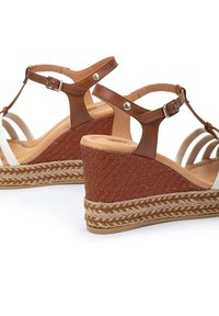 Sandalias de cuña de cuero marrón con textura trenzada, correas blancas, hebilla ajustable y detalles de cuerda trenzada en la plataforma.