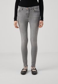Jeans skinny de mezclilla gris con un diseño de cinco bolsillos, botón de cobre y un ligero desgaste. Llevados con flats negros con tachas y calcetines estampados.