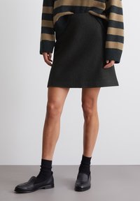 Gonna nera a trapezio realizzata in tessuto testurizzato, abbinata a un maglione oversize a righe. Le calzature includono mocassini neri e calze alla caviglia.