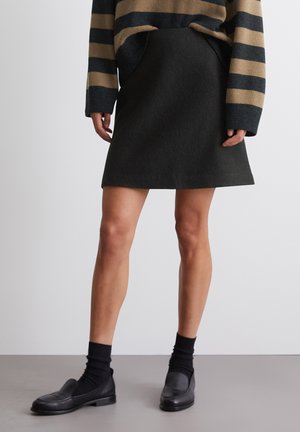 Black, A-line skirt made of textured fabric, paired with a striped oversized sweater. Footwear includes black loafers and ankle socks.