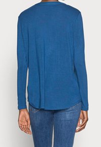 Rundhals-Langarmshirt aus einem einfarbigen, dunkelblauen Stoff. Weicher Textil mit abgerundetem Saum und minimalistischer Gestaltung. Kombiniert mit Denim-Jeans.