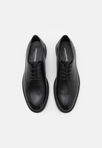 Scarpe di pelle nera con una finitura liscia, punta rotonda e con una chiusura con lacci. Presentano dettagli in cucitura e una suola testurizzata per una migliore aderenza.