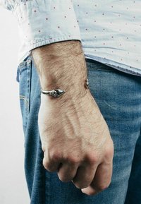 Silver bracelet in a serpent design, featuring detailed scales and a tapered tail, worn on a wrist, against a light background.