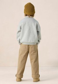 Grauer Sweatshirt, beigefarbene Hose mit umgeschlagenem Saum und eine senfgelbe gestrickte Mütze. Weiche Texturen mit einfachem Design und geradem Schnitt.
