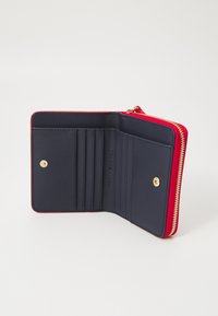 Portefeuille rouge zippé avec intérieur bleu marine, comportant des emplacements pour cartes et une fermeture à bouton pression. Texture lisse et détails en matériel doré.