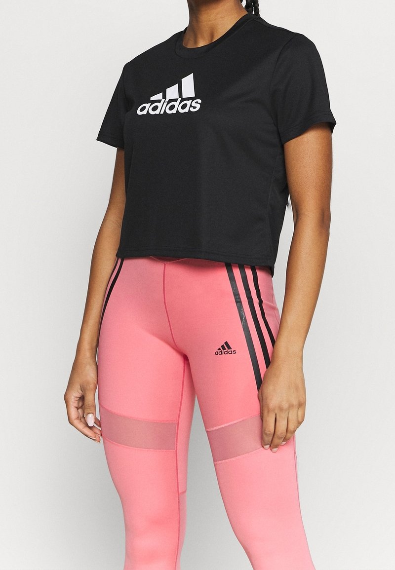 Černé krátké tričko s bílým logem „adidas“, doplněné růžovými legínami s černými pruhy a síťovanými panely.