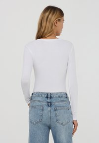 Top bianco a maniche lunghe realizzato in tessuto leggero, abbinato a jeans a vita alta di un blu chiaro con tasche posteriori e una classica texture in denim.