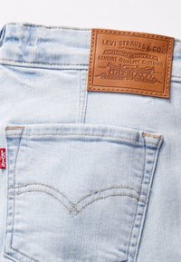 Poche arrière d’un jean en denim bleu clair avec une étiquette rouge Levi’s et une écusson en cuir marron de la marque Levi Strauss & Co. au-dessus de la poche.