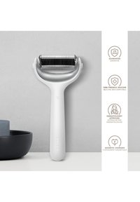 Dermaroller blanc avec des aiguilles en métal, debout verticalement sur une surface à côté d'un bol noir et du savon, avec les principales caractéristiques listées à droite.