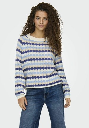 Häkelsweater in blau, creme und beige gestreift; mit einem runden Ausschnitt und rippenförmigen Bündchen. Getragen mit dunkelblauen Jeans.