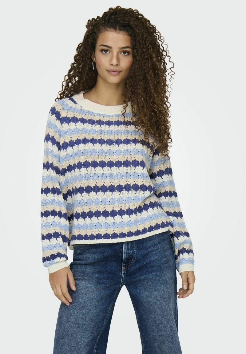 Virkat och stickat tröja i blå, kräm och beige ränder; har en rund halsringning och ribbade ärmslut. Bärs tillsammans med mörkblå jeans.