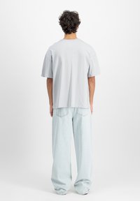 Svijetlosiva pamučna majica s opuštenim krojem, kratkim rukavima i ravnim rubom, u kombinaciji sa svijetloplavim širokim trapericama.