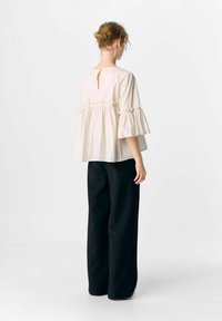Blouse beige clair avec des manches bouffantes, détail de trou de serrure au dos et taille froncée, associée à un pantalon noir à jambes larges. Texture lisse, design décontracté.