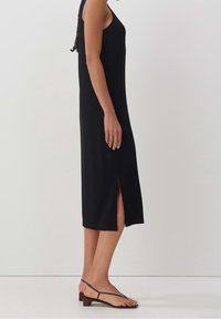 Svart ribbad midiklänning med en sidoklyvning, med tunna axelremmar och en figurnära siluett. Buren med platta minimalistiska sandaler.