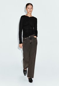 Top nero a maniche lunghe con texture arricciata, scollatura rotonda, abbinato a pantaloni morbidi marrone scuro e scarpe nere slip-on.