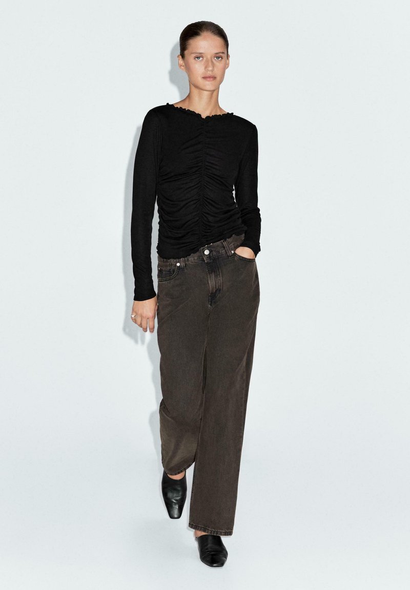 Top nero a maniche lunghe con texture arricciata, scollatura rotonda, abbinato a pantaloni morbidi marrone scuro e scarpe nere slip-on.