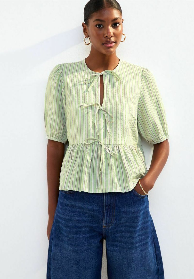 Lichtgroene gestreepte blouse met korte pofmouwen, striksluiting bij de hals, uitlopende zoom, gecombineerd met wijde spijkerbroek.