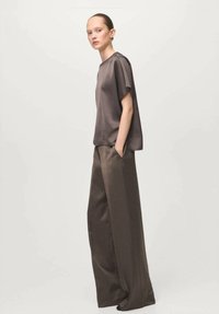 Bluza maro cu mâneci scurte, combinată cu pantaloni largi, cu talie înaltă, cu textură netedă și croială lejeră. Design minimalist, tonuri neutre.