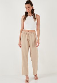 Lichtbeige linnen wijde broek met een elastische tailleband en een trekkoord; gecombineerd met een witte geribbelde crop top en beige sandalen met bandjes.