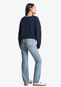 Temno modra pletena jopica z ohlapnim krojem in rebrastim ovratnikom, v kombinaciji s svetlo modrimi hlačami naravnega kroja in belimi supergami s svetlo rjavimi podplati.