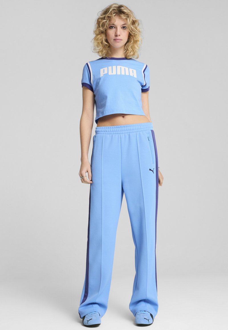 Lyseblå cropped t-shirt med "PUMA" logo, parret med matchende blå bukser med marineblå side-striber og lynlåslommer.