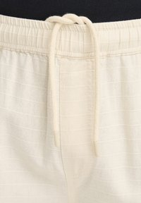 Shorts beige texturés avec une taille élastique et un cordon de serrage. Présente des rayures subtiles et un tissu doux pour le confort.