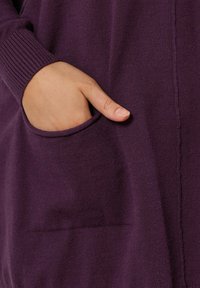 Fioletowy sweter z dzianiny z ściągaczami przy rękawach oraz boczną kieszenią, charakteryzujący się miękką teksturą i nowoczesnym designem.