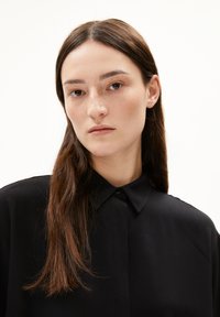 Schwarzes Hemd mit kurzer Knopfleiste, klassischem Kragen, glatter Textur und langen Ärmeln. Fokussiert auf die Vorderansicht des Hemdes, minimalistischem Design.