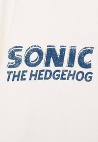 Tessuto bianco con un testo blu audace che recita "SONIC THE HEDGEHOG", con un aspetto texturizzato e leggermente usurato.