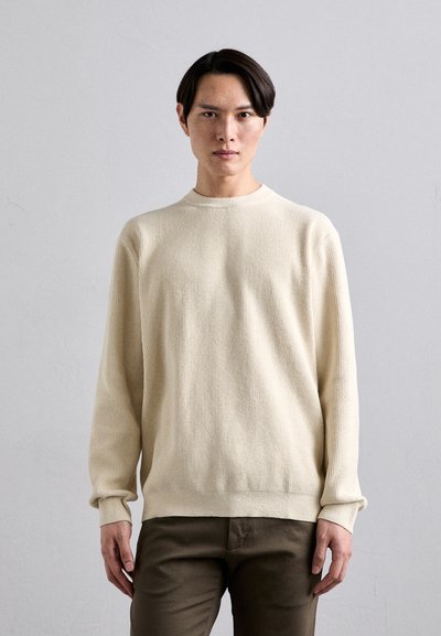 Pull crème texturé à manches longues et col rond, associé à un pantalon vert olive. Motif de tissu lisse et côtelé.