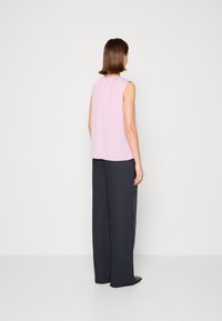 Top sin mangas de color rosa claro con un corte holgado, combinado con pantalones de pierna ancha de color azul oscuro; diseño minimalista sin patrones o herrajes visibles.