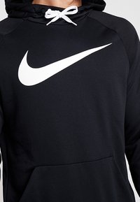 Hoodie noir avec un logo swoosh blanc de Nike. Caractéristiques : capuche à cordon, manches longues et poche frontale. Texture lisse et coupe athlétique.