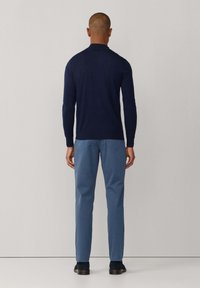 Granatowy sweter z długim rękawem i wysokim kołnierzem, skomponowany z jasnoniebieskimi spodniami. Gładka faktura, dopasowany krój i minimalne detale.