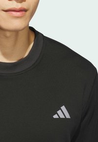 Black athletic sweatshirt with a round neckline, featuring a grey Adidas logo on the chest and smooth, textured fabric.