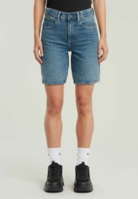 Lichte blauwe denim shorts met een hoge taille, voorzien van vijf zakken en een rauwe zoom. Draag ze met zwarte sneakers en witte sokken.
