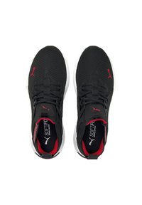 Baskets de sport noires avec un upper en mesh, accents rouges, col rembourré et semelle blanche, présentant un motif texturé et un détail de logo.