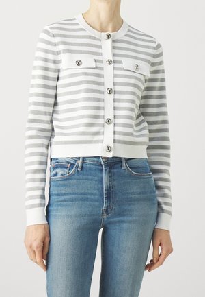 Femme portant un cardigan boutonné à rayures horizontales blanches et grises avec des boutons argentés, associé à un jean bleu taille haute.