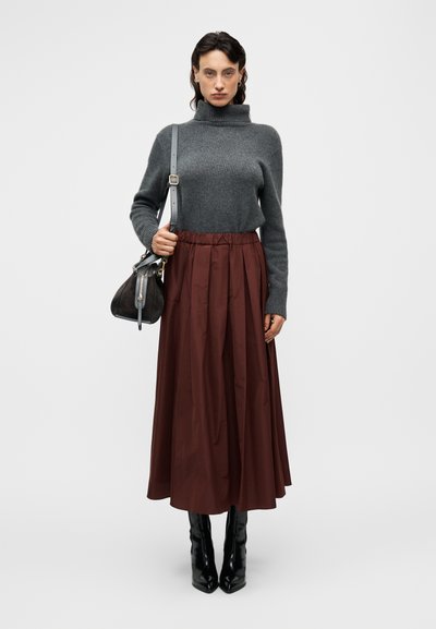 Σκούρο γκρι πουλόβερ με ψηλό λαιμό συνδυασμένο με ένα μπουργουνδί πλισέ μίντι φόρεμα. Τα αξεσουάρ περιλαμβάνουν μια μαύρη τσάντα ώμου και λαμπερά μαύρα μποτάκια με τακούνι.