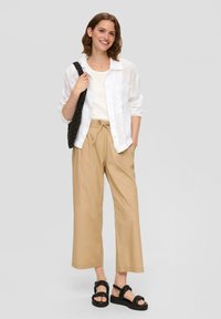 Witte linnen blouse, beige hoge taillebroek met een trekkoord in de taille, zwarte sandalen met kettingaccenten, een gestructureerde zwarte tas.