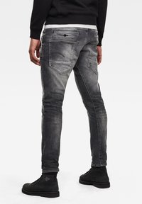 Šedé džíny s úzkým střihem, s kapsami na zadní straně a jemným vyblednutím. Vytvořeno v kombinaci s černými botami, což zdůrazňuje uvolněný design.