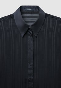 Schwarzes Hemd mit Knöpfen, feinen vertikalen Streifen, einem spitzen Kragen und einer kleinen dekorativen Verzierung am obersten Knopf.