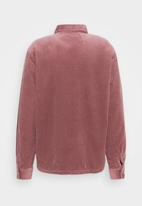 Camisa de pana en color rosa empolvado con textura de canalé vertical, cuello y mangas largas. Presenta detalles de botones en los puños de las mangas.