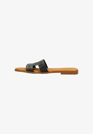 Zwarte leren slipper met uitsnijdingen, een platte tan kleurige zool en minimale hardware details. Soepele textuur en comfortabele pasvorm.