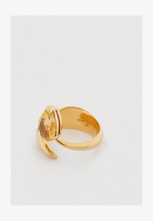 Gold ring with a pear-shaped yellow gemstone set in a twisted band. The band features a smooth finish and subtle curved accents.