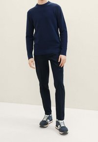 Marinblå texturerad tröja, åtsittande design, i kombination med mörka byxor och marinblå sneakers med vita snören och sula.